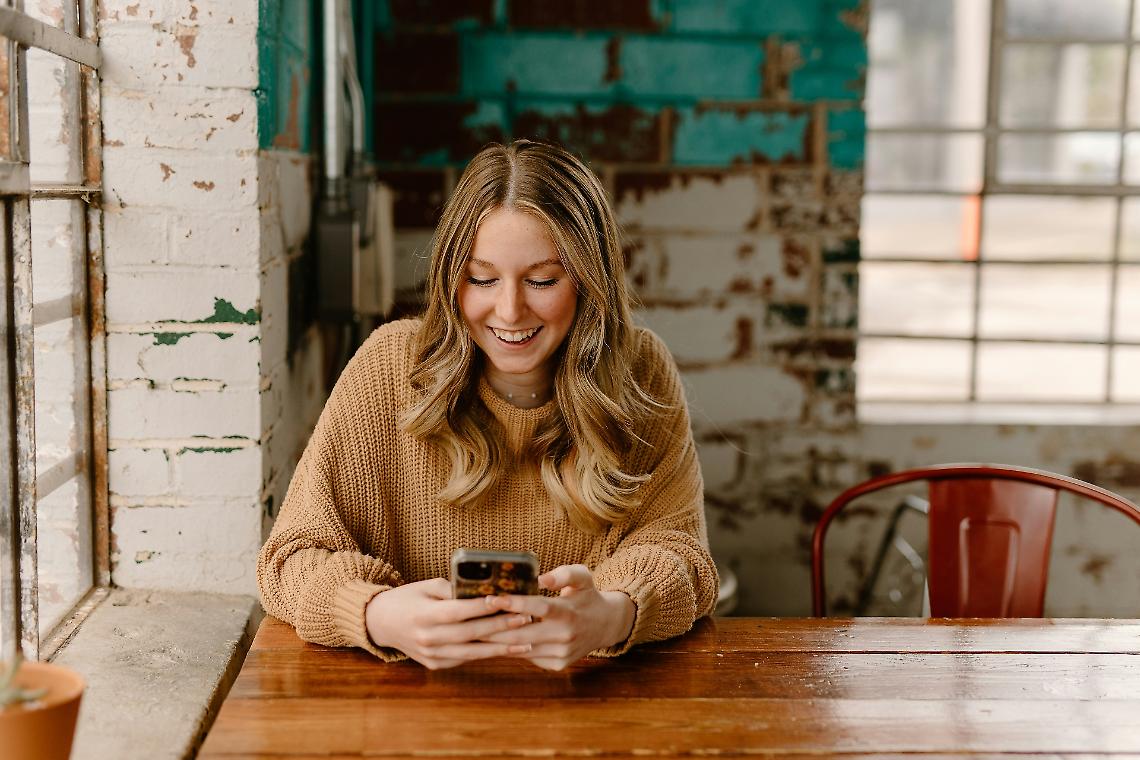 Una donna seduta a un tavolo guarda la foto del suo cellulare – Immagine di caffè gratuita su Unsplash