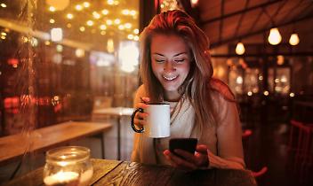 Una persona seduta a un tavolo che beve e sorride mentre guarda il telefono - Immagine d'archivio gratuita