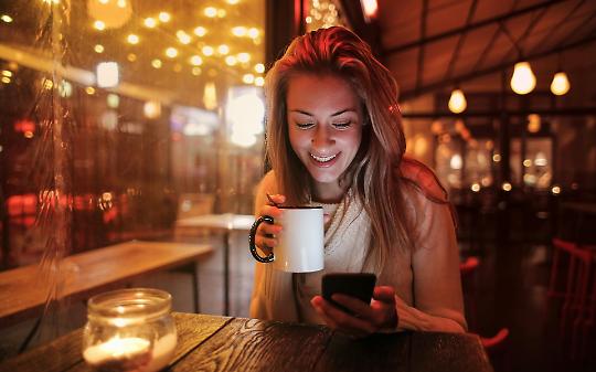 Una persona seduta a un tavolo che beve e sorride mentre guarda il telefono - Immagine d'archivio gratuita